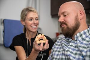 Dr. Anderson showing a patient a dental implant model as she determines the cost of his dental implant procedure.