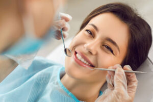 Woman smiling during a dental checkup as a dentist uses a mirror and dental tool to examine her teeth.